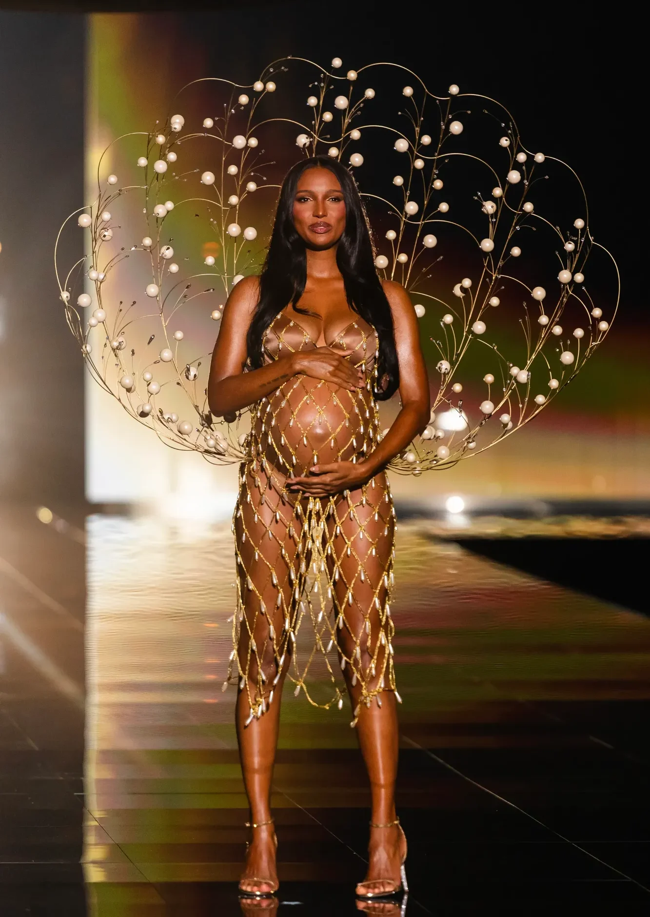 Schwangere Frau in eleganter, glitzernder Robe mit auffälligem Kopfschmuck auf dem Laufsteg.